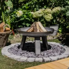 Ein moderner Grillplatz im Garten mit Feuerschale, Holzkorb und üppiger Bepflanzung. Perfekt für laue Sommerabende.