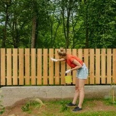 Frau streicht neuen Holzzaun, ein DIY-Projekt für den Garten.