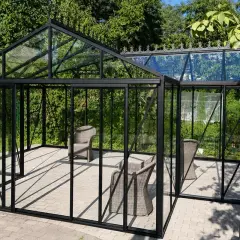Eine Orangerie ist ein Glashaus, das Pflanzen Schutz bietet. Hier stehen Korbstühle in einer modernen Orangerie mit schwarzem Rahmen.