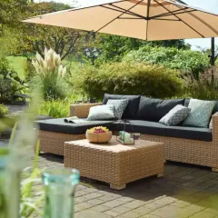 Gemütliche Lounge-Ecke im Garten unter Sonnenschirm. Coole Gartenideen einfach umgesetzt mit Rattansofa, Couchtisch und Obstschale.