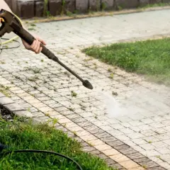 Person mit Hochdruckreiniger entfernt Unkraut zwischen Pflastersteinen dauerhaft.