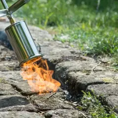 Ein Brenner bekämpft hartnäckiges Unkraut auf einem gepflasterten Weg. Flammen lodern aus dem Metallgerät und vernichten unerwünschte Pflanzen.