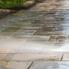 Hochdruckreiniger sprüht Wasser auf ein schmutziges Betonpflaster, um es zu reinigen.