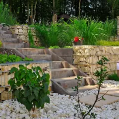 Moderner **Garten anlegen** mit Stufen aus Beton und Gabionenmauern. Gräser und Büsche schmücken die Terrassen.