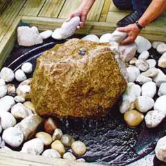 Ein Quellstein im Garten: Ideen für ein beruhigendes Wasserspiel mit Natursteinen und Holzdeck.