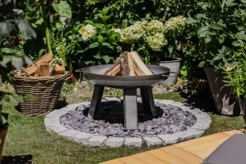 Ein moderner Grillplatz im Garten mit Feuerschale, Holzkorb und üppiger Bepflanzung. Perfekt für laue Sommerabende.