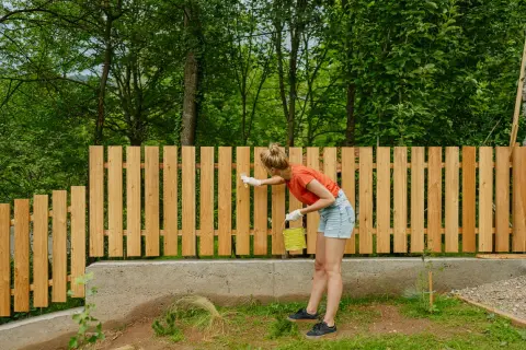 Frau streicht neuen Holzzaun, ein DIY-Projekt für den Garten.