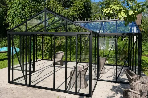 Eine Orangerie ist ein Glashaus, das Pflanzen Schutz bietet. Hier stehen Korbstühle in einer modernen Orangerie mit schwarzem Rahmen.