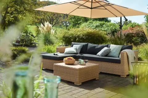 Gemütliche Lounge-Ecke im Garten unter Sonnenschirm. Coole Gartenideen einfach umgesetzt mit Rattansofa, Couchtisch und Obstschale.
