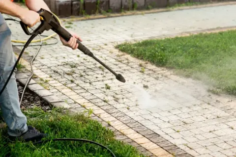 Person mit Hochdruckreiniger entfernt Unkraut zwischen Pflastersteinen dauerhaft.