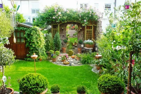 Ein moderner kleiner Garten im Reihenhaus mit Steinbogen, Rosen, Schuppen und viel Grün.