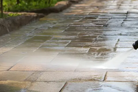 Hochdruckreiniger sprüht Wasser auf ein schmutziges Betonpflaster, um es zu reinigen.