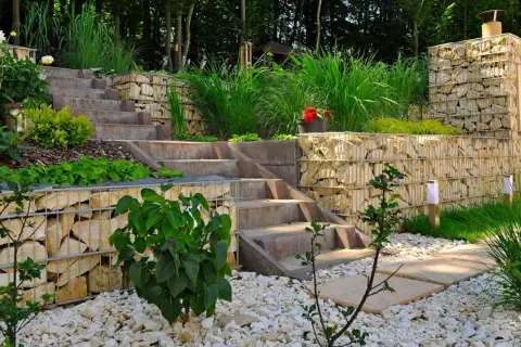 Moderner **Garten anlegen** mit Stufen aus Beton und Gabionenmauern. Gräser und Büsche schmücken die Terrassen.