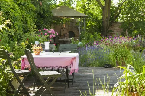 Ein idyllischer Freisitz mit Tisch und Stühlen, umgeben von blühenden Rosen, Lavendel und einem Pizzaofen.