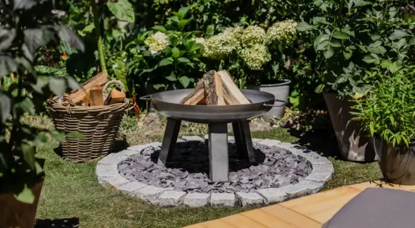 Ein moderner Grillplatz im Garten mit Feuerschale, Holzkorb und üppiger Bepflanzung. Perfekt für laue Sommerabende.
