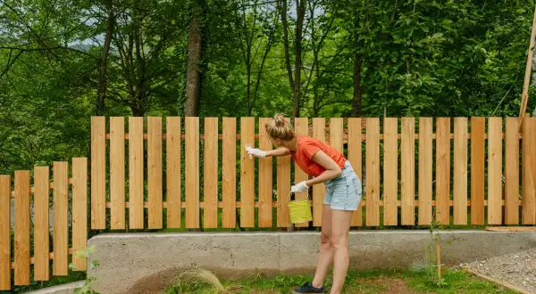 Frau streicht neuen Holzzaun, ein DIY-Projekt für den Garten.