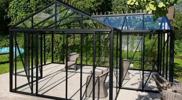Eine Orangerie ist ein Glashaus, das Pflanzen Schutz bietet. Hier stehen Korbstühle in einer modernen Orangerie mit schwarzem Rahmen.