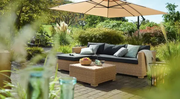 Gemütliche Lounge-Ecke im Garten unter Sonnenschirm. Coole Gartenideen einfach umgesetzt mit Rattansofa, Couchtisch und Obstschale.