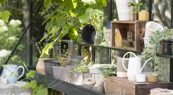 Schöne Landhausgarten Ideen: Pflanzen, Gießkannen und Deko-Häuschen in einem Gewächshaus.