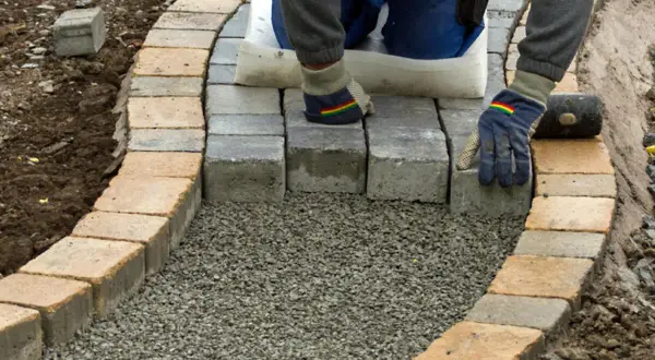 Arbeiter legt mit Handschuhen und Werkzeug einen neuen Gartenweg an, Stein für Stein.