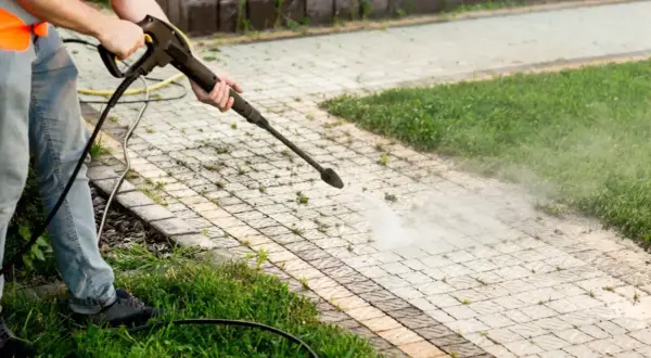 Person mit Hochdruckreiniger entfernt Unkraut zwischen Pflastersteinen dauerhaft.