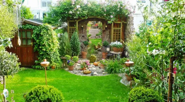 Ein moderner kleiner Garten im Reihenhaus mit Steinbogen, Rosen, Schuppen und viel Grün.