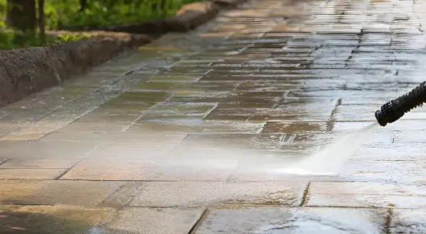 Hochdruckreiniger sprüht Wasser auf ein schmutziges Betonpflaster, um es zu reinigen.