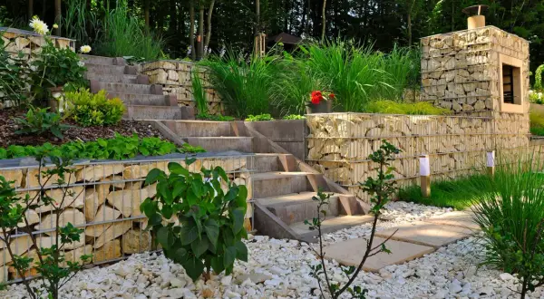 Moderner **Garten anlegen** mit Stufen aus Beton und Gabionenmauern. Gräser und Büsche schmücken die Terrassen.