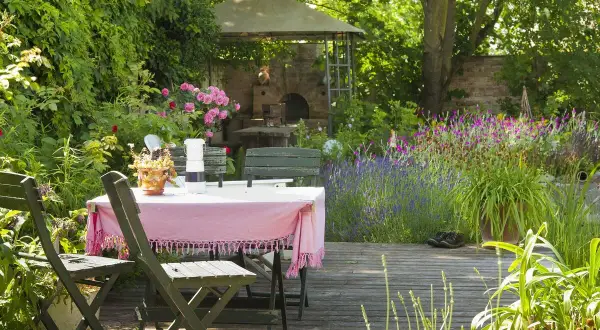 Ein idyllischer Freisitz mit Tisch und Stühlen, umgeben von blühenden Rosen, Lavendel und einem Pizzaofen.