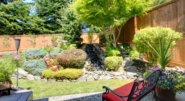 Ein sehr kleiner Garten mit einem Wasserfall, üppiger Bepflanzung und einer roten Bank.
