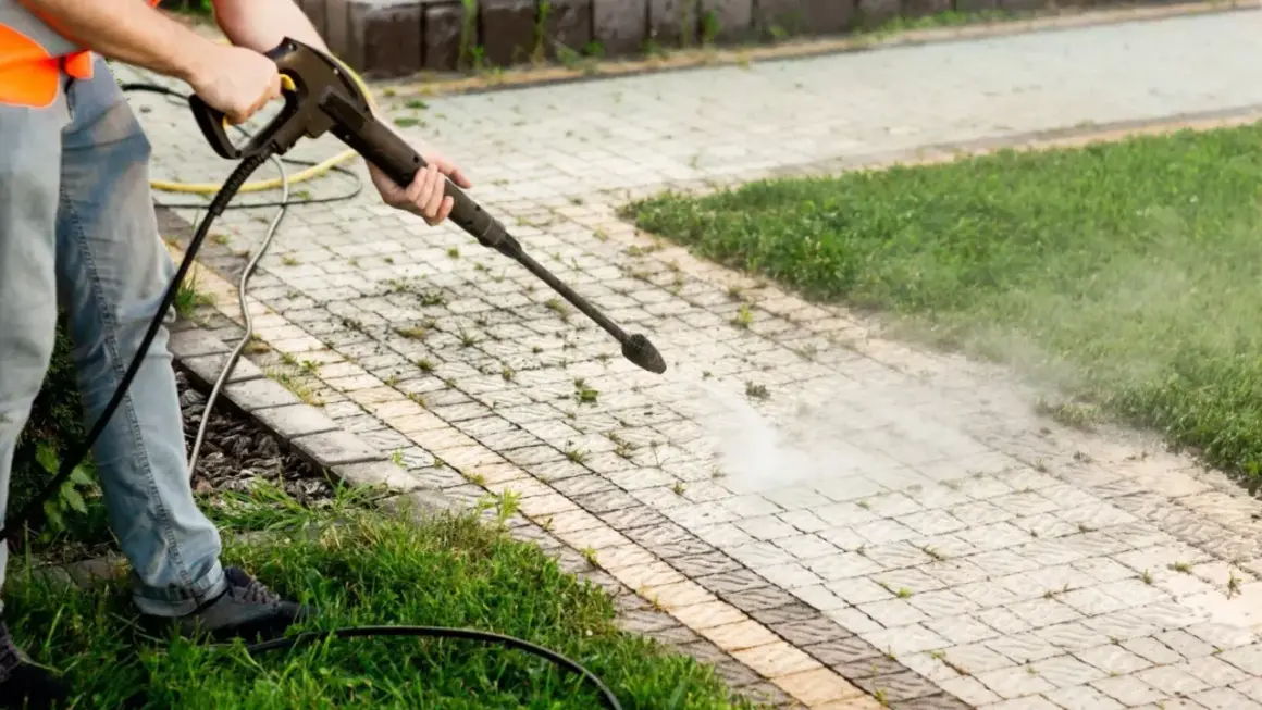 Person mit Hochdruckreiniger entfernt Unkraut zwischen Pflastersteinen dauerhaft.