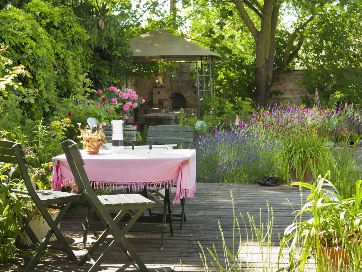Ein idyllischer Freisitz mit Tisch und Stühlen, umgeben von blühenden Rosen, Lavendel und einem Pizzaofen.