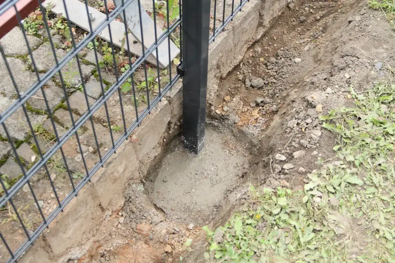 Beim doppelstabmattenzaun aufbauen wird ein Pfosten in Beton gesetzt. Der frisch gegossene Beton f&uuml;llt das ausgehobene Loch um den Pfosten.