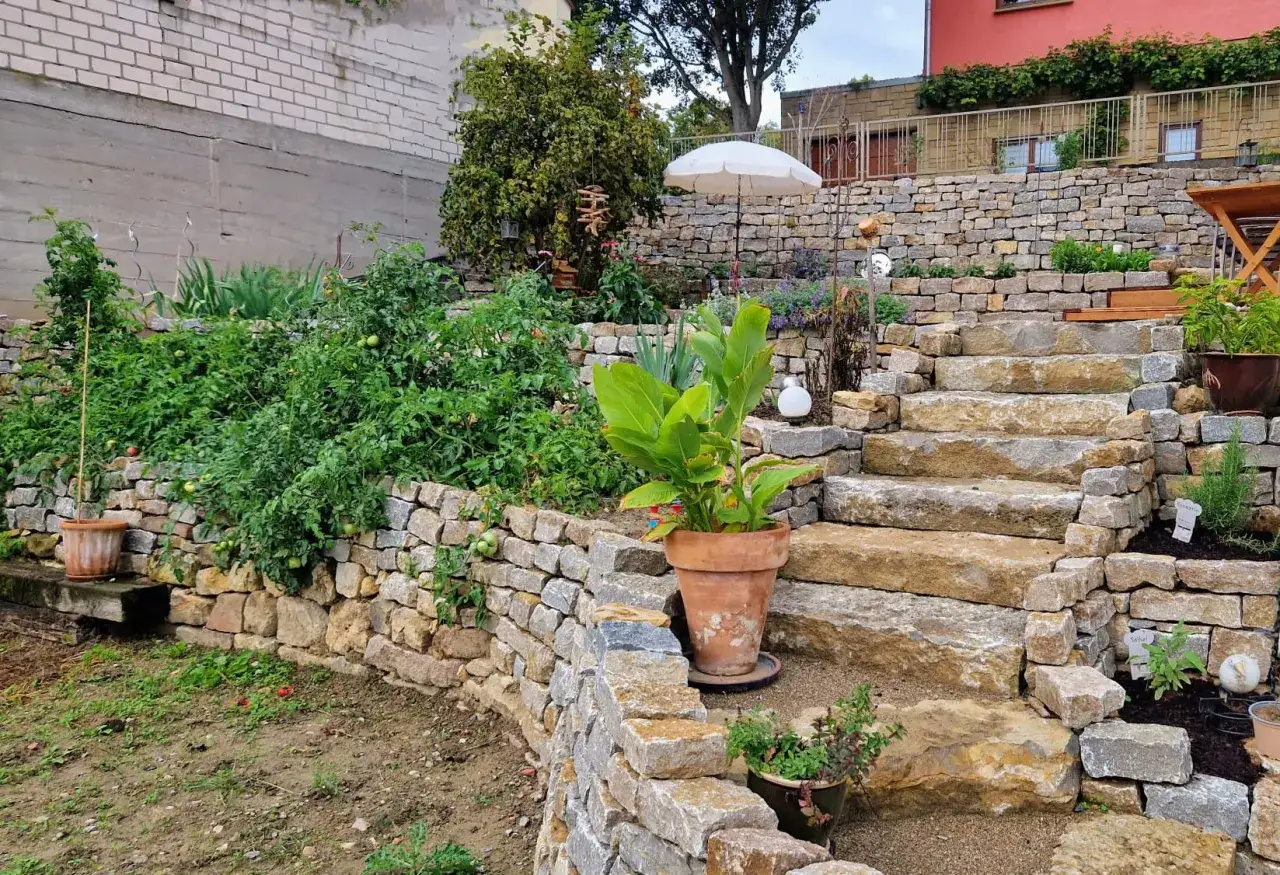 Eine wunderschöne Gartentreppe, die zeigt, wie man eine natursteinmauer bauen kann. Üppige Pflanzen und ein kleiner Sonnenschirm machen den Garten zum Paradies.
