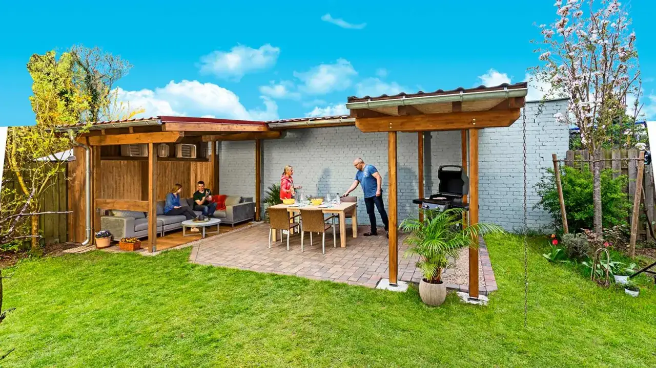 Gem&uuml;tlicher Grillplatz im Garten mit &uuml;berdachter Lounge-Ecke und Essbereich. Ein Mann bereitet den Grill vor, w&auml;hrend Freunde entspannen.