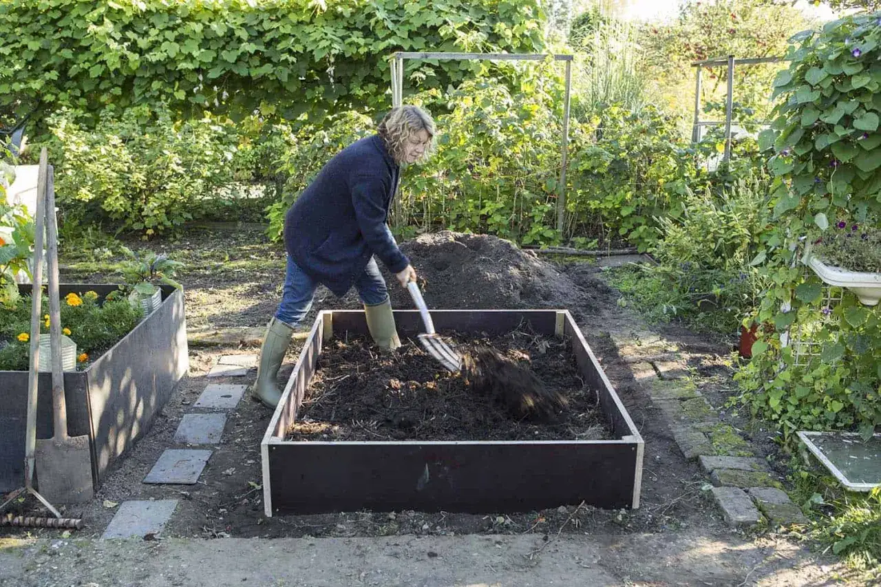 Frau bearbeitet Erde mit einer Gabel f&uuml;r den Aufbau eines Hochbeets.