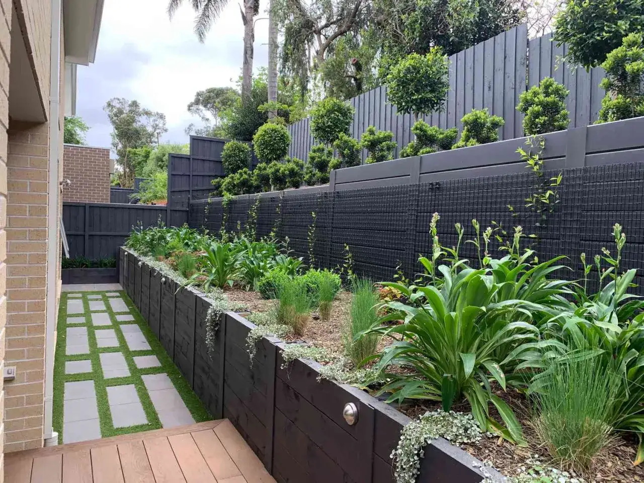 Moderne Gartengestaltung mit dunklen Holzelementen und &uuml;ppiger Bepflanzung. Tolle Ideen mit Pflanzsteinen f&uuml;r eine strukturierte und gr&uuml;ne Oase.