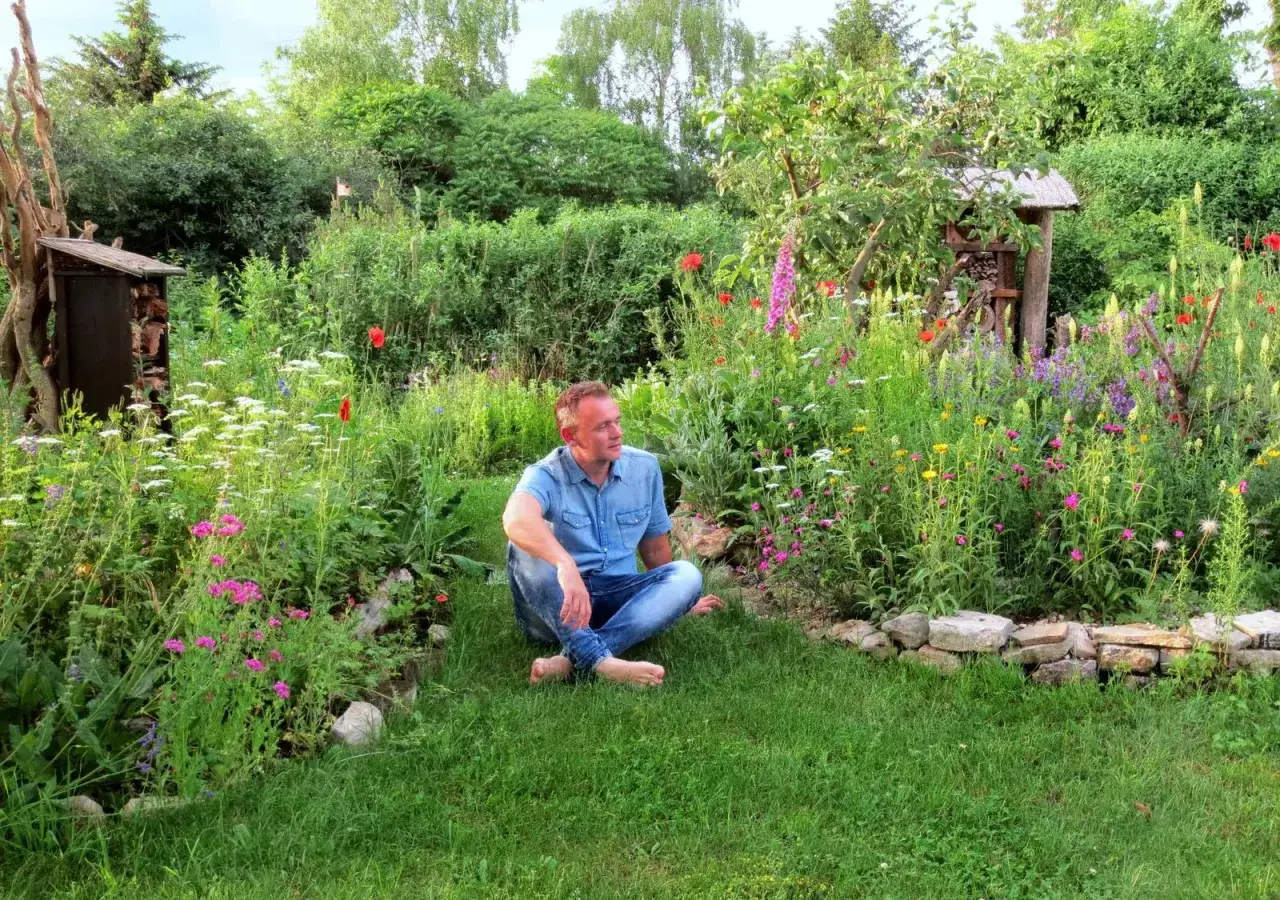 Mann sitzt in einem bl&uuml;henden Garten. Tolle wildgarten ideen f&uuml;r ein naturnahes Paradies.