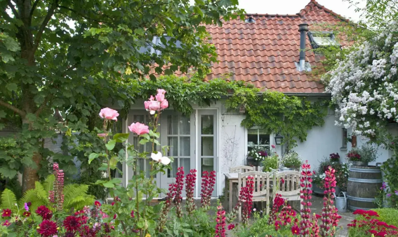 Bl&uuml;hender Landhausgarten mit Rosen, Lupinen und einem Sitzbereich. Tolle Landhausgarten Ideen f&uuml;r ein idyllisches Zuhause.
