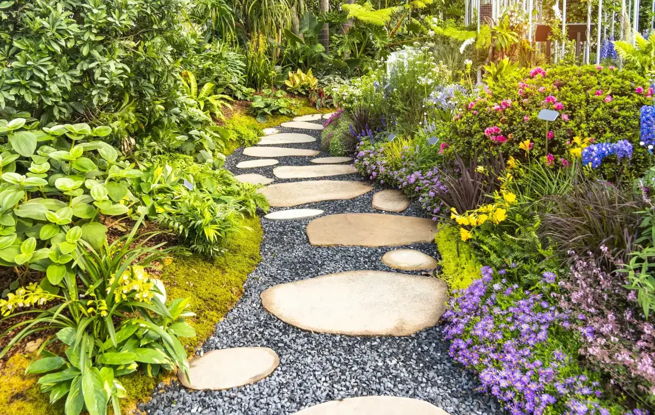 Ein malerischer Gartenweg aus Trittsteinen und Kies schlängelt sich durch üppige grüne Pflanzen und bunte Blumen.