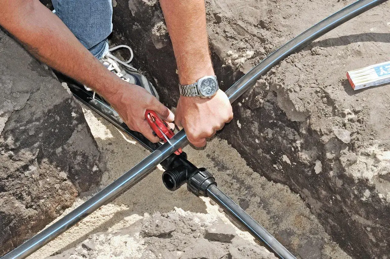 Mann verlegt eine neue wasserleitung im garten. Mit einem Rohrschneider wird das schwarze Rohr zugeschnitten, um es an ein T-St&uuml;ck anzuschlie&szlig;en.