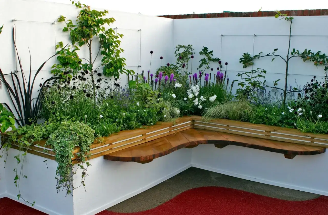 Moderne Kleingarten Ideen: Eine geschwungene Holzbank l&auml;dt zum Verweilen ein, umgeben von &uuml;ppigen, bl&uuml;henden Beeten mit lila und wei&szlig;en Blumen.