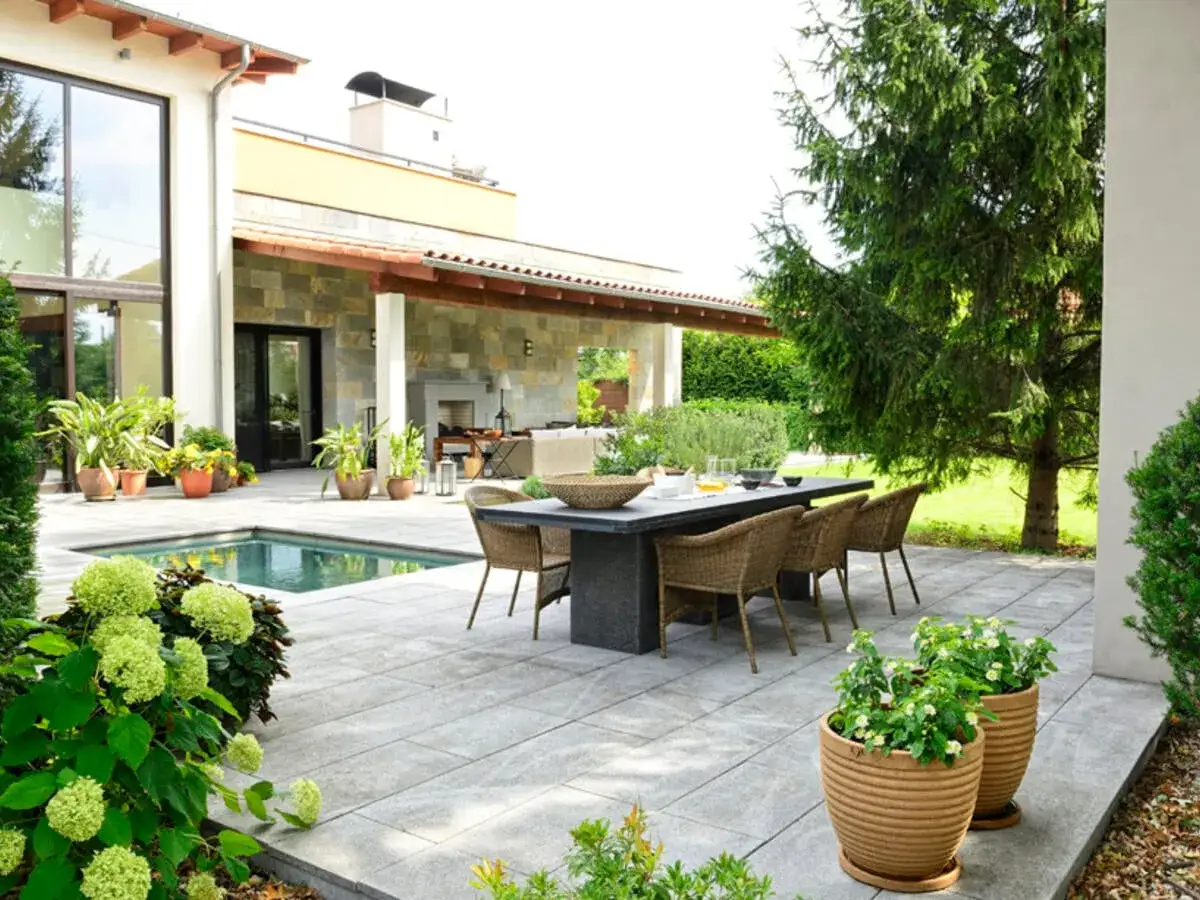 Moderne Terrassenumrandung Ideen: Ein Essbereich mit Korb-St&uuml;hlen und Steintisch l&auml;dt zum Verweilen ein, daneben ein kleiner Pool und &uuml;ppige Pflanzen.