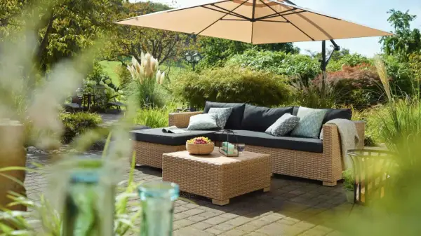 Gemütliche Lounge-Ecke im Garten unter Sonnenschirm. Coole Gartenideen einfach umgesetzt mit Rattansofa, Couchtisch und Obstschale.