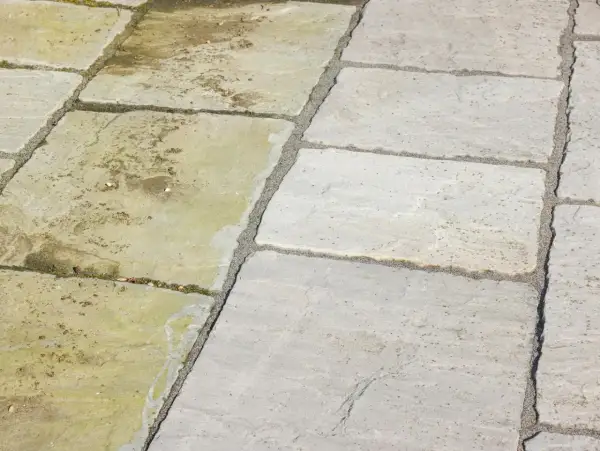 Terrassenplatten reinigen: Eine Hälfte der Platten ist sauber und hellgrau, die andere ist schmutzig und grünlich.