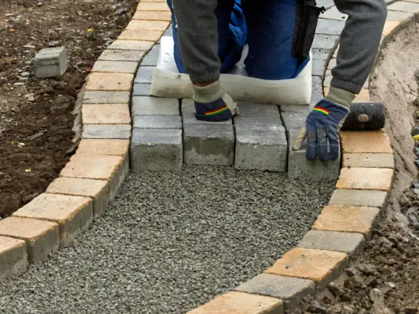 Arbeiter legt mit Handschuhen und Werkzeug einen neuen Gartenweg an, Stein für Stein.