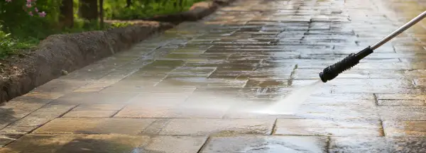 Hochdruckreiniger sprüht Wasser auf ein schmutziges Betonpflaster, um es zu reinigen.