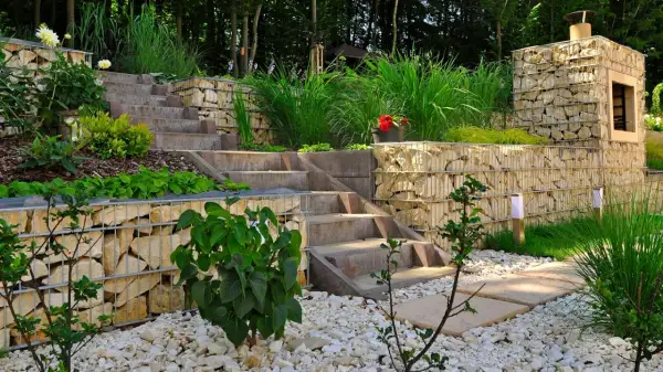 Moderner **Garten anlegen** mit Stufen aus Beton und Gabionenmauern. Gräser und Büsche schmücken die Terrassen.